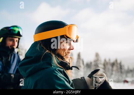 Lächelnde Frau mit Skibrille, während sie im Winter die Kaffeetasse in der Hand hält Stockfoto