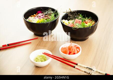 Zwei Sack-Salate mit Rindfleisch und Thunfisch in einer Schüssel auf einem Restauranttisch. In einer Schüssel neben Essstäbchen und Ingwer mit Wasabi Salate anstoßen. Asiatischer Salat Stockfoto