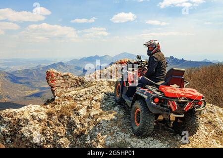 Mann im Helm sitzt auf ATV Quad Bike in den Bergen Stockfoto
