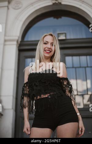 Junge hübsche blonde Frau lächelt und posiert vor einem Gebäude Stockfoto