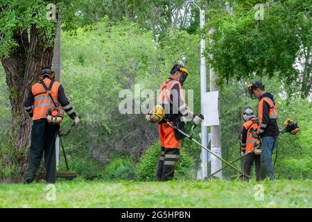 Rasenmähen und Rasenmähen. Drei Arbeiter mähen Rasenmäher mit Rasenmähern im Park. Stockfoto