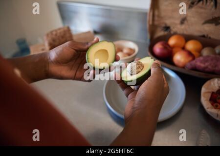 Afrikanischer Mann schneidet in seiner Küche eine Avocado in die Hälfte Stockfoto