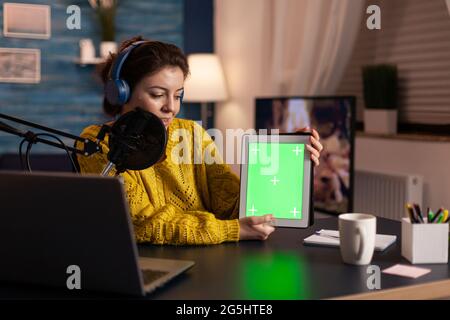 Influencer hält ein Tablet mit grünem Bildschirm und zeichnet neue Podcast-Serien für das Publikum auf. Broadcast Show Host Streaming von Live-Inhalten für Social Media mit Mochup, Chroma-Key, izolated Desktop. Stockfoto