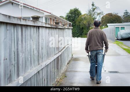 Ein Mann schiebt eine leere Schubkarre auf die Betoneinfahrt und säubert den Garten Stockfoto