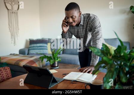 Afrikanischer Geschäftsmann, der von zu Hause aus mit seinem Handy und Tablet arbeitet Stockfoto