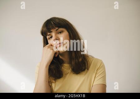 Junge Frau mit der Hand am Kinn vor der weißen Wand Stockfoto