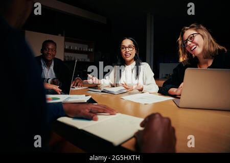 Glückliche, vielfältige Gruppe von Geschäftsleuten, die am Tisch sitzen und im Büro zusammenarbeiten Stockfoto