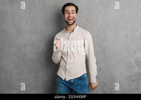 Glücklich schöner junger Mann in lässigem Outfit feiert Erfolg isoliert auf grauem Hintergrund Stockfoto