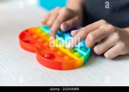 Bunte Antistress Sinnesspielzeug Fidget Push Pop es in die Hände des Kindes. Das Mädchen drückt ihren Finger auf das Gummispielzeug, das es auf den Tisch knallt. Stockfoto