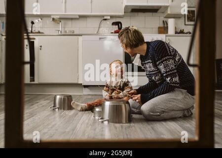 Mädchen, das Mutter ansieht, während sie zu Hause in der Küche Utensilien mit Essstäbchen spielt Stockfoto