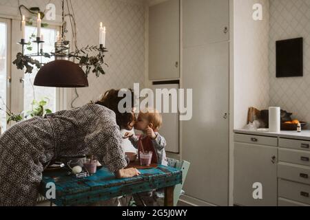 Liebevolle Mutter küsst Tochter sitzen am Esstisch in der Küche Stockfoto