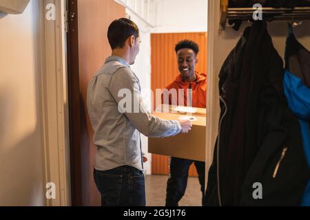 Lächelnder junger Lieferer, der dem männlichen Kunden am Eingang des Hauses das Paket gab Stockfoto