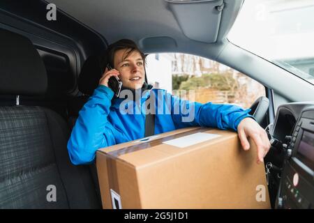 Junge Frau, die mit dem Paket im Lieferwagen sitzt und mit dem Mobiltelefon spricht Stockfoto