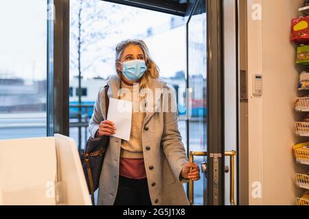 Weibliche Kundin mit mittlerem Erwachsenenalter, die während der COVID-19 in das Einzelhandelsgeschäft eintrat Stockfoto