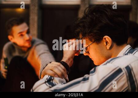 Junger Mann, der die Hand eines besorgten männlichen Freundes auf dem Balkon hält Stockfoto