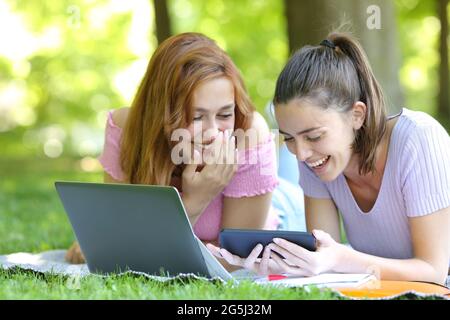 Glückliche Studenten, die sich Online-Videos auf dem Smartphone ansehen, lachen und liegen im Park auf dem Rasen Stockfoto