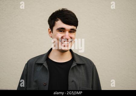 Fröhlicher junger Mann mit schwarzen Haaren an der beigen Wand Stockfoto