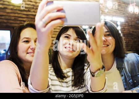 Drei Freundinnen in einem Café, die Spaß haben und Selfies machen - fröhliche Freundinnen, die sich am Telefon Filmen - Konzept von Freundschaft, Freude und Vertrauen Stockfoto