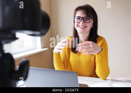 Eine Bloggerin unterhält ihren Kanal und kommuniziert über eine Online-Übertragung mit den Abonnenten - EINE junge Frau in gelbem Kleid führt eine Webina Stockfoto