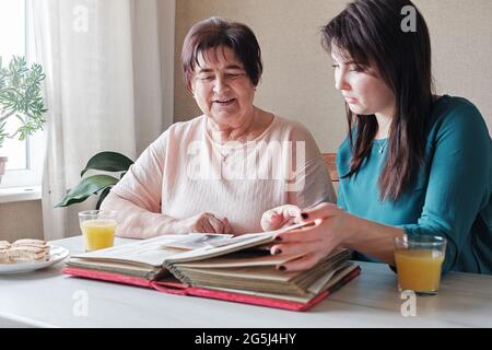 Großmutter und Tochter beobachten ein Familienalbum mit alten Fotos zusammen - Generationen in einer gemeinsamen Aktivität verbinden - eine ältere und eine junge Frau ta Stockfoto