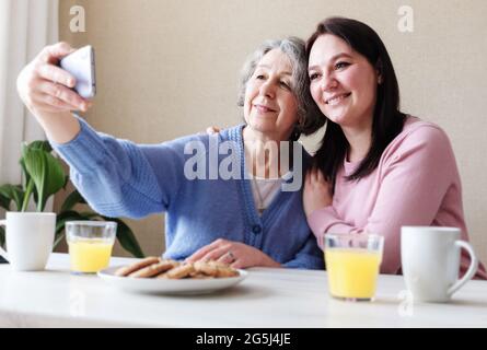 Ältere pensionierte Frau mit ihrer erwachsenen Tochter, die während des Frühstücks ein Selfie am Tisch machte - das Konzept von Saatgutwerten und Freundschaft in der Familie Stockfoto