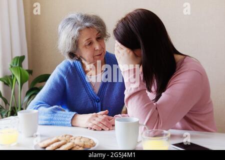 Eine ältere Frau tröstet ihre Tochter, wenn sie krank ist und unter Stress steht - EIN Rentner leistet einem jungen Mädchen psychologische Hilfe - die Stockfoto