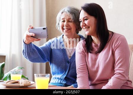 Eine ältere Mutter und eine Erwachsene Tochter machen ein Selfie zu Hause - Großmutter und Enkelin kommunizieren - Freundschaft zwischen einem älteren und einem jungen Menschen Stockfoto