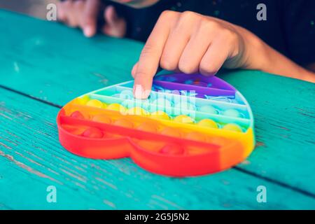 Bunte Antistress Sinnesspielzeug Fidget Push Pop es in die Hände des Kindes. Das Mädchen drückt ihren Finger auf das Gummispielzeug, das es auf den Tisch knallt. Stockfoto