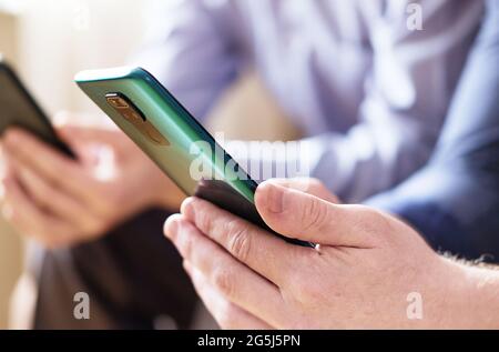 Zwei junge Männer halten Telefone in den Händen und schauen sich Inhalte in sozialen Netzwerken an - EIN Smartphone in der Hand eines Mannes aus der Nähe und ein verschwommener Hintergrund - die c Stockfoto