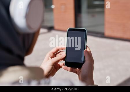 Nahaufnahme einer modernen Frau aus dem Nahen Osten mit Smartphone in einer Stadt, die von Sonnenlicht beleuchtet ist, Fokus auf weißen Bildschirm, Kopierraum Stockfoto