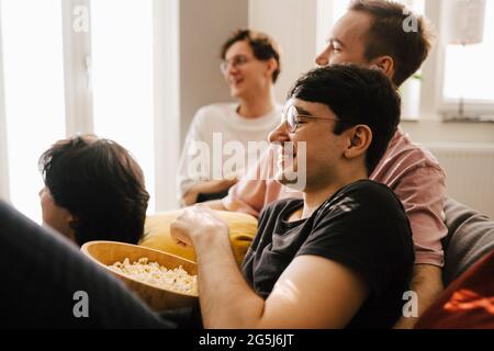 Multiethnische männliche Freunde, die Popcorn essen, während sie im Wohnzimmer Sport treiben Stockfoto