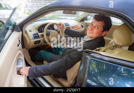 Lächelnd auf den männlichen Kamerastreiber in den Vierzigern, der in einem alten Cabriolet mit geöffneter Tür sitzt. Stockfoto