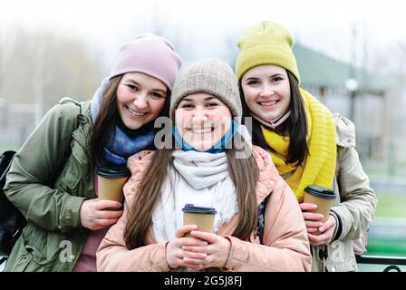 Mädchen in abgesenkten Gesichtsmasken schauen auf die Kamera und lächeln - Mädchen haben Spaß in der Stadt und posieren vor der Kamera - Freundinnen sind Trinker Stockfoto