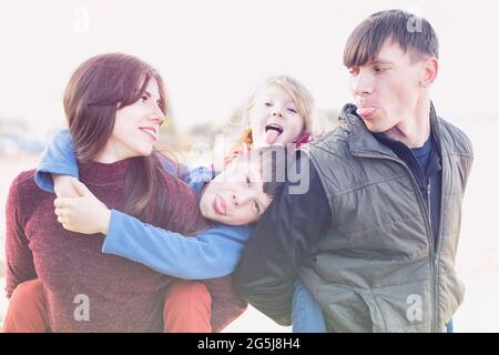 Eltern und zwei Kinder haben Spaß zusammen - Familie der Narren um und zeigen Zunge - Papa Mama und zwei Kinder umarmen zusammen glückliches Familienkonzept Stockfoto