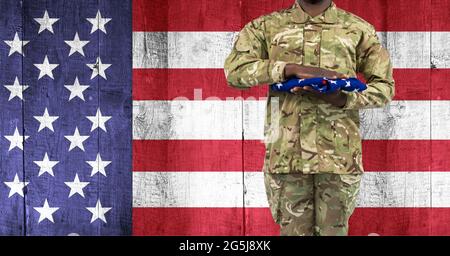 Zusammensetzung des Mittelteils des Soldaten mit Hand auf gefalteter amerikanischer Flagge, gegen amerikanische Flagge Stockfoto