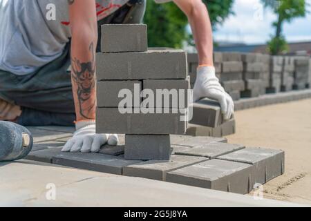 Nahaufnahme der Hände eines Bauarbeiters, die an einem sonnigen Sommertag Pflasterplatten im Freien auf einem vorbereiteten Fundament legen Stockfoto