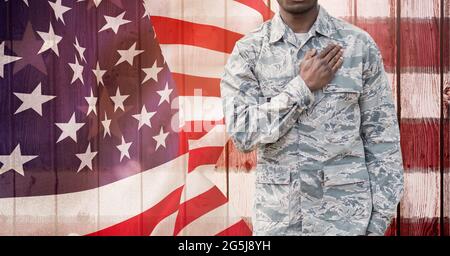 Zusammensetzung des Mittelteils des männlichen Soldaten mit der Hand auf dem Herzen, gegen das Blasen der amerikanischen Flagge Stockfoto