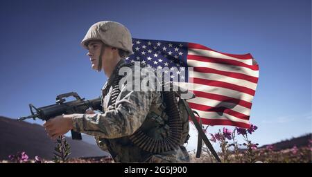 Zusammensetzung eines männlichen Soldaten mit Waffe, mit winkender amerikanischer Flagge, gegen den blauen Himmel Stockfoto