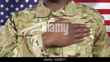 Zusammensetzung des Mittelteils des männlichen Soldaten mit Hand auf Herz, gegen die amerikanische Flagge Stockfoto