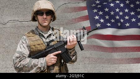 Zusammensetzung eines männlichen Soldaten, der eine Sonnenbrille mit einem Gewehr an einer Betonwand und einer amerikanischen Flagge trägt Stockfoto