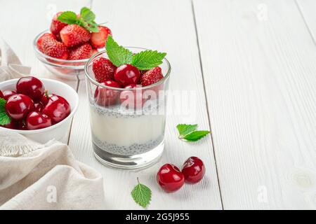 Dessert mit Milch, Chiasamen und frischen Beeren und Früchten auf weißem Hintergrund. Cremepudding mit Erdbeeren und Kirschen. Stockfoto