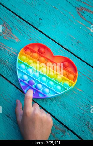 Bunte Antistress Sinnesspielzeug Fidget Push Pop es in die Hände des Kindes. Das Mädchen drückt ihren Finger auf das Gummispielzeug Pop es auf den Tisch. Vertikale Foto Stockfoto