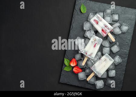 Drei Eiscremes mit Chiasamen und Erdbeeren auf einem Holzstab auf schwarzem Hintergrund. Stockfoto