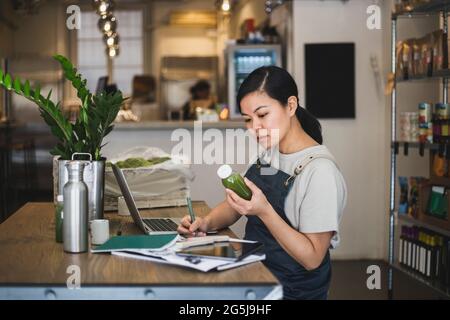 Asiatische weibliche Unternehmerin schreiben, während Saftflasche im Laden halten Stockfoto