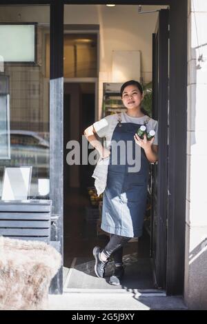 Asiatische Angestellte, die im Laden vor der Tür steht Stockfoto