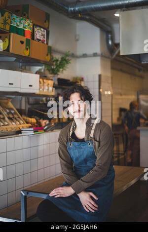 Porträt eines jungen männlichen Unternehmers, der im Geschäft auf dem Tisch sitzt Stockfoto