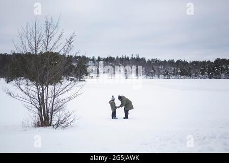 Frau hilft Tochter mit Jacke, während sie im Winter auf Schnee steht Stockfoto