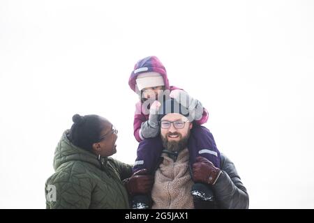 Glückliche Frau, die im Winter die Tochter auf der Schulter des Mannes sieht Stockfoto