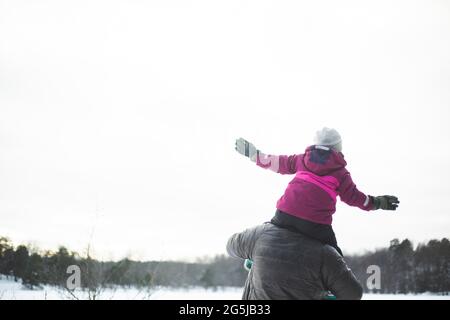 Rückansicht des Vaters, der seine Tochter im Winter auf den Schultern trägt Stockfoto