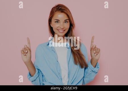 Glückliche junge Frau zeigt mit Zeigefinger nach oben und lächelt Stockfoto